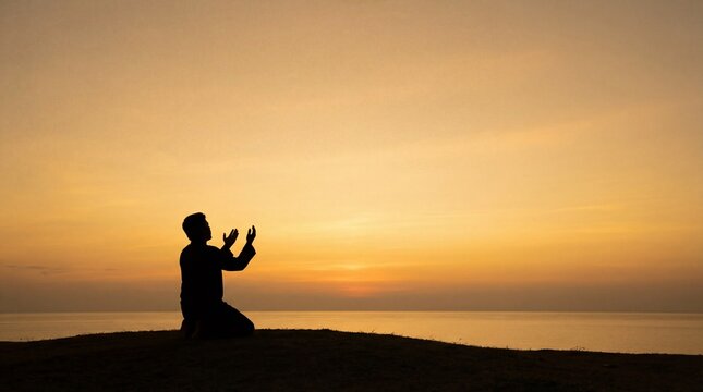 Silhouette of a Muslim man praying on his knees facing the ocean at sunset.