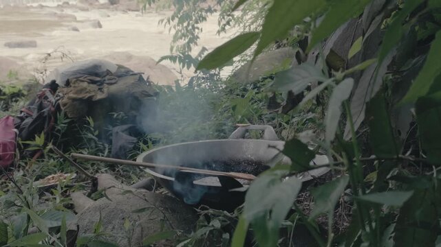 Smooth Cinematic Zoom-in of Sizzling Frying in a Wok Over Open Fire by a Rushing River