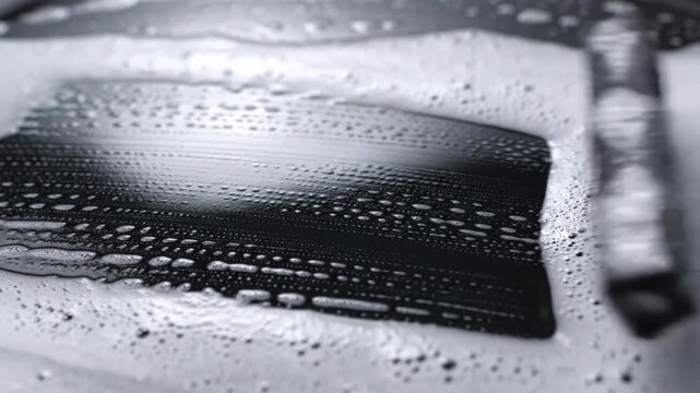 A squeegee cleans a dark surface covered in white soap foam. It effectively removes suds, revealing a clean, shiny area.