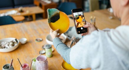 Hands of a woman photographing her products with a smartphone in a ceramics studio