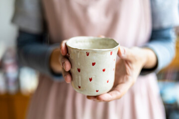 Woman's hands holding a handmade mug with a heart-shaped pattern
