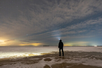 Man with headlamp standing on frozen sea ice at Kaberneeme beach Estonia under starry sky exploring melting winter ice landscape. © Dmitri