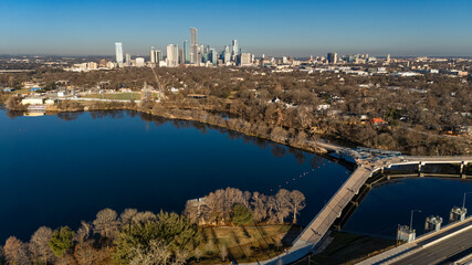 Fototapeta premium Aerial drone photograph showing parkland and shoreline along Lady Bird Lake in East Austin with downtown Austin’s skyline rising beyond. 
