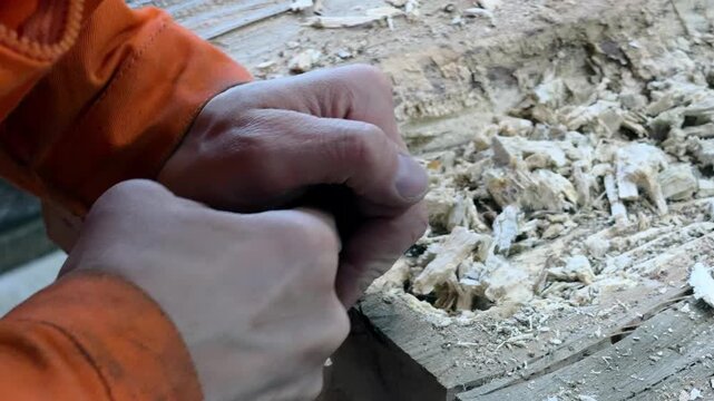 A carpenter in overalls chiselling a wooden slab in a woodworking shop. A person working. Tools, chisel, hands. Woodworking. Sawdust, wood chips. Real people. Lifestyle, Authentic, Candid