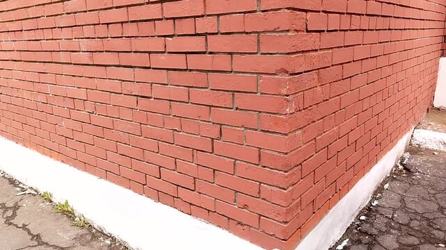 Red brick wall corner with white base, showing texture and pattern of bricks, captured from multiple angles in a well-lit outdoor setting
