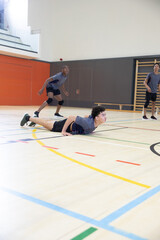 Diverse teenage males practicing on school gym court in gray shirts black shorts knee pads