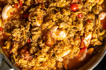The process of making paella. Close-up: Chicken pieces with tomatoes and seafood are fried in a pan. Background
