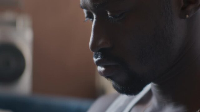 Focused Black man looking down thoughtfully, nodding his head to music rhythm as counting money in living room at home. Close-up view