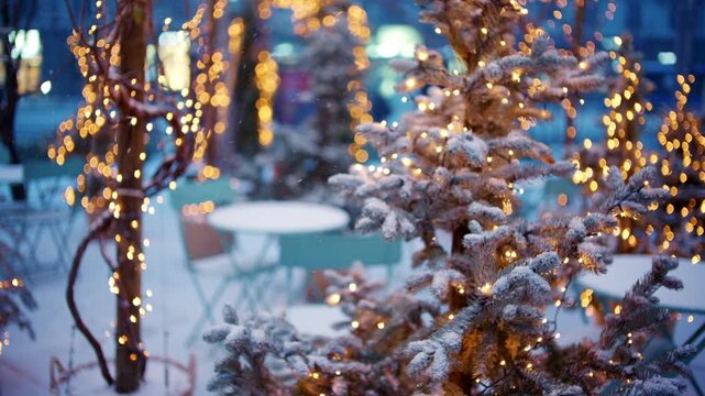 Close up of a small Christmas tree covered in snow and decorated with warm string lights outdoors