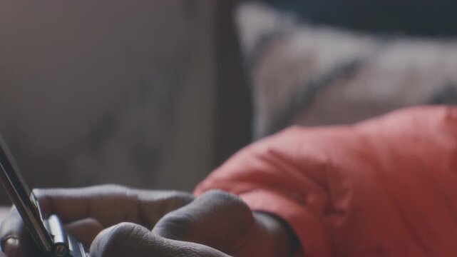 Close up view of young Black man dialing number and talking on flip phone as sitting in sunlit room at home. Tilt-up shot