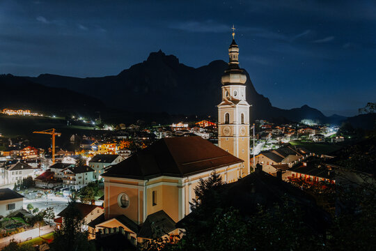 Illuminated Parish Church of Castelrotto at Night &ndash; Traditional Alpine Village Architecture with Steeple under Dark Blue Sky in South Tyrol