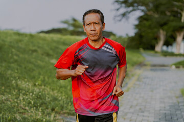 Portrait of asian senior man runner jogging in the morning at public park. Helathy lifestyle exercise, active seniors concept.