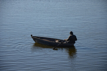 Lone fisherman in a rowing boat on a calm river at sunrise. 