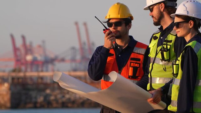 Maritime engineering personnel reviewing architectural blueprints at industrial port. Logistics supervisor coordinating terminal operations via radio transceiver.