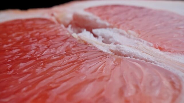 Half of fresh grapefruit rotating at black background. Organic healthy food concept. Close-up in 4K, UHD