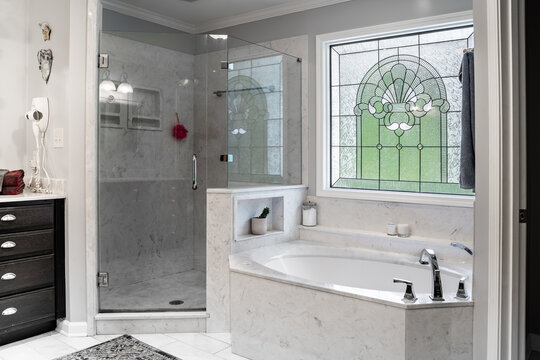 Modern master bathroom with white marble tub and stained glass window