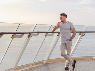 Fashionable man with a glass of drink standing on the empty deck of a cruise ship against the backdrop of sea waves. Sunny day. Chill lifestyle, luxury travel. Perfect for holiday and travel themes © Svetlana