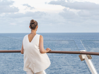 Cute woman standing on the empty deck of a cruise liner against the backdrop of sea waves. Sunny day. Vacation, travel concept. Chill lifestyle, luxury travel. Perfect for holiday and travel themes © Svetlana
