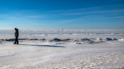 Wonderful view of the frozen sea coast in winter, man walks along the snowy seashore, rocky coast