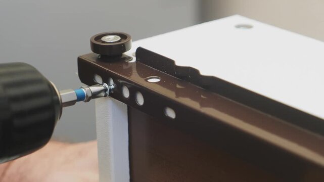 Human hands use a screwdriver to screw in the screws and assemble the furniture. The middle plan.