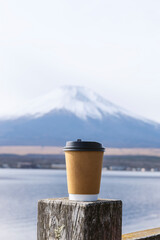 Takeaway paper coffee cup on a wooden post with blurred Mount Fuji in the background.