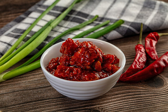 Spicy red chili pickle in a white bowl on a rustic wooden table with fresh ingredients