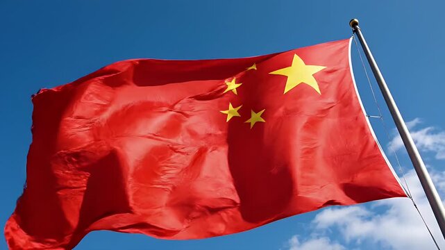 Chinese Flag Waving Against Blue Sky - The Chinese national flag, featuring a red background with five yellow stars, is displayed waving prominently in the wind.