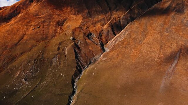 aerial canyon with golden mountain slopes, windswept terrain carved by seasonal streams with narrow gullies and scree fields, deep shadows creating bold contrast and rich texture, minimal vegetation