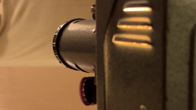 A vintage film projector whirs as it feeds a celluloid strip through its lens. The soft, warm glow from the machine creates a nostalgic and peaceful atmosphere in the dim room.