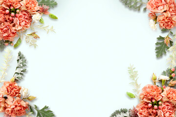 Fresh carnation flowers, leaves and berries arrangement on light blue background, top view. Floristic frame decoration. Natural floral background.