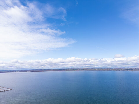 Scenic aerial view capturing the expansive blue waters of lake simcoe extending to the distant shoreline beneath a clear sky with scattered white clouds, located in georgina, ontario, canada