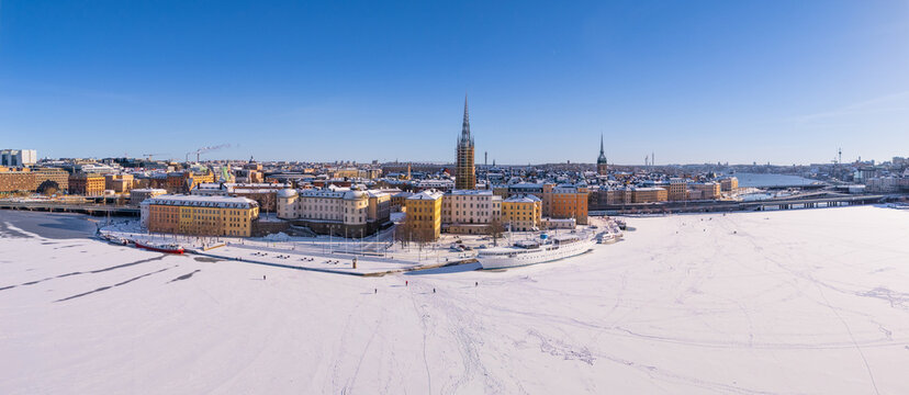 Wintry Stockholm old town, with ice and snow, and people walking on the lake, clear blue sky, Riddarholmen church, panoramic aerial view