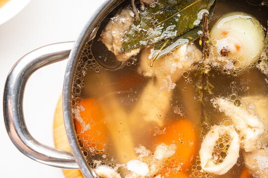 Meat or chicken broth with bay leaf, carrots, and onions simmers in a saucepan. View from above. Background with broth texture. Soup making process.