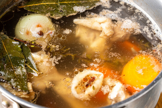 Meat or chicken broth with bay leaf, carrots, and onions simmers in a saucepan. View from above. Background with broth texture. Soup making process.