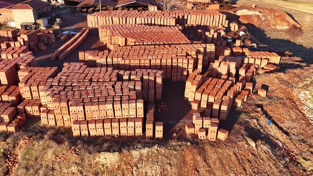 Red construction bricks neatly stacked in an open-air warehouse. Building materials and industrial stock concept in the light of sunset.