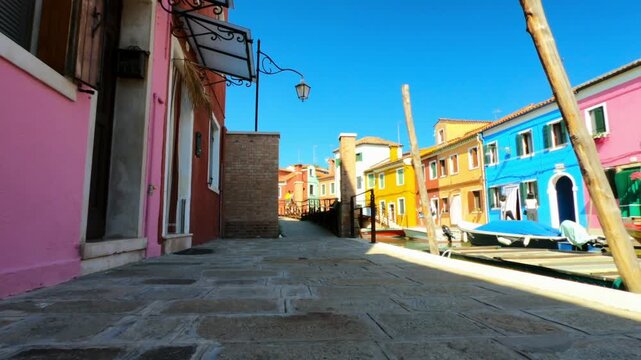 A view along Riva dei Santi and Fondamenta di Terranova footpaths in Burano. Colorful houses and boats moored in the waterway.