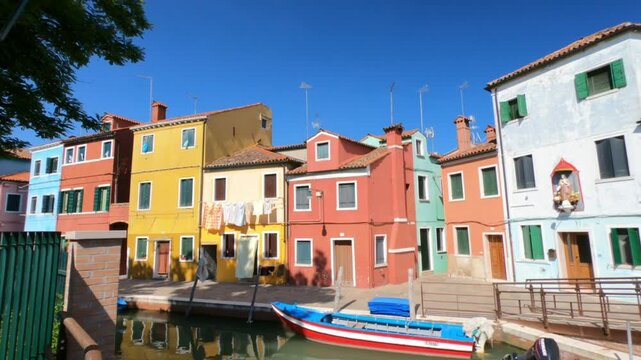Burano / Venice / Italy - June 23, 2019: WALKING SHOT  A view along Riva dei Santi and Fondamenta di Terranova footpaths in Burano. Colorful houses and boats moored in the waterway.