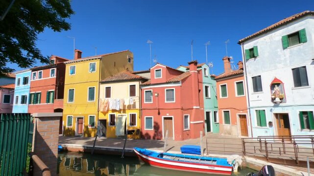 Burano / Venice / Italy - June 23, 2019: WALKING SHOT  A view along Riva dei Santi and Fondamenta di Terranova footpaths in Burano. Colorful houses and boats moored in the waterway.