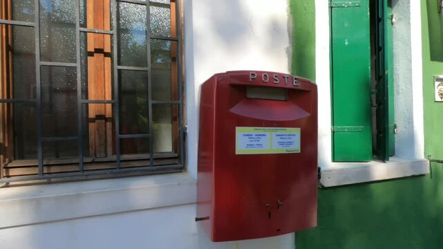 Burano / Venice / Italy - June 23, 2019: SLOW MOTION - Italian Post Office Post at Fondamenta di Terranova, Burano. Red postal box for public use.