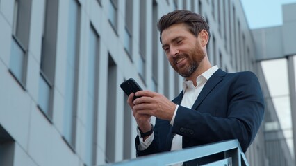 Stylish adult Caucasian business man holding mobile phone in city smiling mature businessman male...
