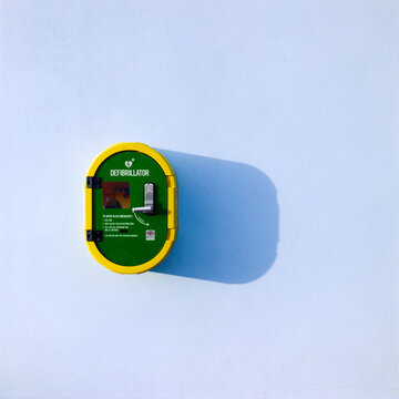 Defibrillator safe, defib safe, on a plain blue wall outdoors with a shadow, life saving equipment, public access defibrillator
