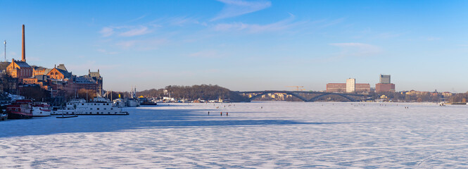 Panoramic view of the frozen lake M&auml;laren in Stockholm, with people walking on ice, with Kungsholmen, S&ouml;dermalm and frozen boats