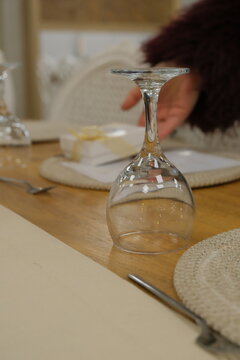 Rustic wedding table setting with beige gift box, menu card, wine glasses, and woven placemat on a wooden table.
