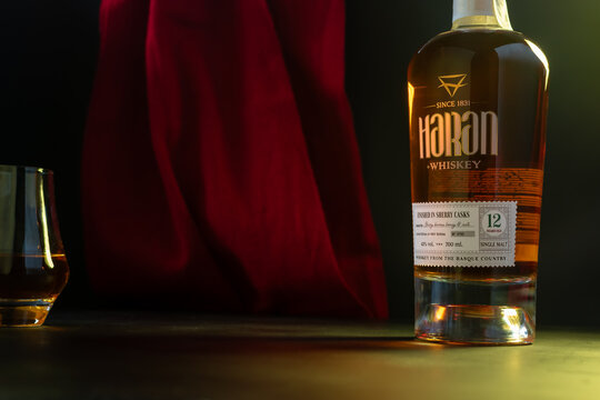 Haran 12 Years Old Single Malt Whiskey finished in Sherry Casks. Bottle and glass against deep red fabric drapery on dark moody background. Ukraine, Zhytomyr, February 18, 2026