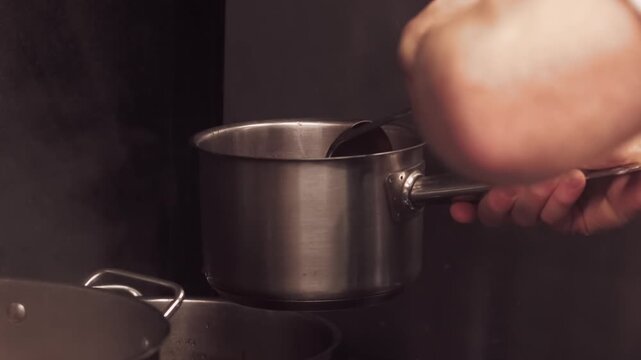 Cooking process. Pouring food. Chef ladling portion of hot borsch from big metal pan. Professional cookware for kitchen electric stove.