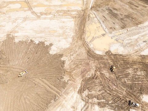 Aerial view of a large construction site showing earthmoving equipment working on a vast area of disturbed ground. With piles of dirt. Muddy puddles. And numerous tracks indicating ongoing development