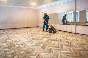 Carpenter worker is sanding polishing wooden parquet floor during renovation