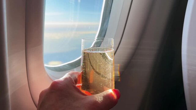 Glass of champagne being held in a person's hand in the business class cabin of an airliner during turbulence 