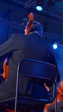 Music Under Lights, Intimate Shot Capturing String Section Under Blue Lighting With Conductor In Background. Media