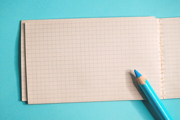 Minimal flat lay of blank grid notebook with blue pencil on pastel background, clean workspace concept for writing, planning, ideas, and productivity.